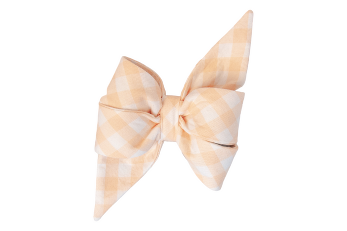 A stylish feminine belle bow made from soft apricot and white checked fabric, featuring two full, rounded loops and sharply tapered tails. The fabric is neatly folded and cinched in the center, creating a crisp, structured look, photographed against a plain white background.