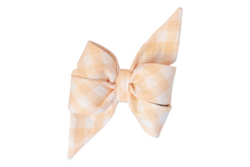 A stylish feminine belle bow made from soft apricot and white checked fabric, featuring two full, rounded loops and sharply tapered tails. The fabric is neatly folded and cinched in the center, creating a crisp, structured look, photographed against a plain white background.