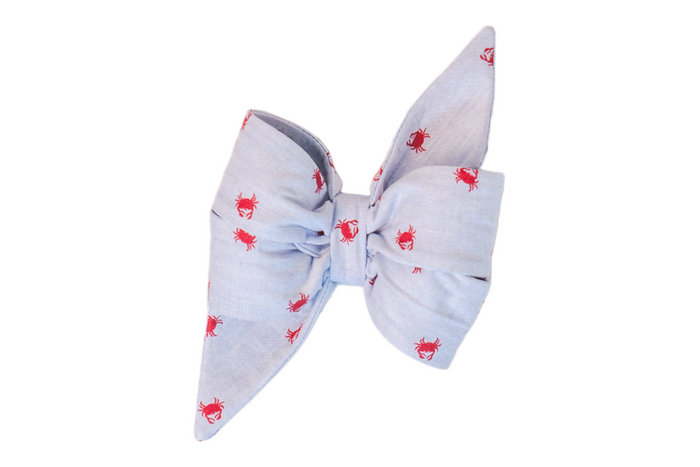 A light blue fabric girl dog belle bow with pointed ends, decorated with a repeating red crab pattern. The bow is neatly folded and structured, adding a nautical-themed flair.